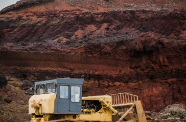 A yellow bulldozer excavating in a rugged red earth quarry under a cloudy sky.